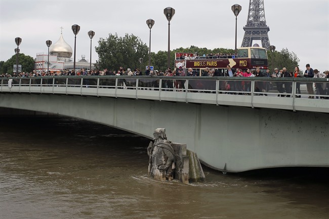 People looking at the floods stand on the Alma bridge by the Zouave statue which is used as a measuring instrument during floods in Paris, France Saturday June 4, 2016. 