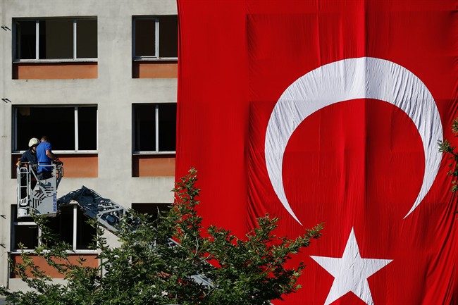 Workers drape a huge Turkish flag on a facade of a building damaged in Tuesday's explosion in Istanbul, Wednesday, June 8, 2016.