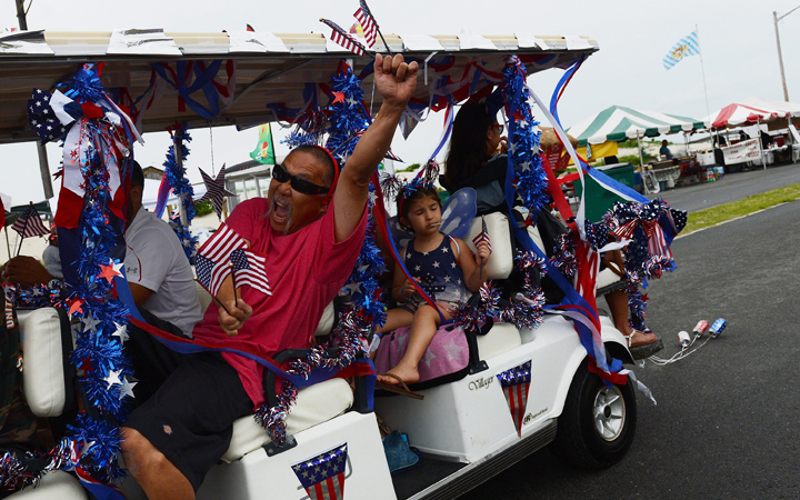 Henry Mayeda waves multiple American flags as he participates in the Fourth of July parade in Cape Charles, Va., on Monday, July 4, 2016. 