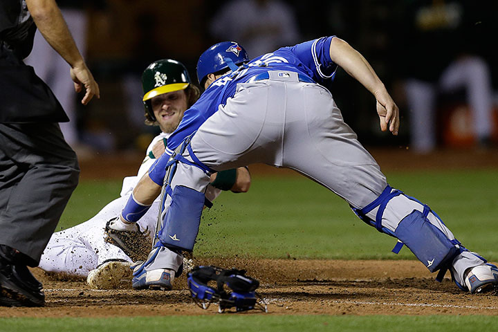 Oakland Athletics' Josh Reddick, rear, scores past Toronto Blue Jays catcher Russell Martin during the seventh inning of a baseball game Friday, July 15, 2016, in Oakland, Calif.