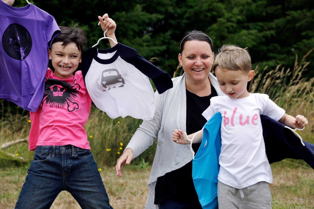 In this Thursday, July 7, 2016, photo, Martine Zoer poses for a photo with her sons Tyler, 8, left, and Tristan, 5, as they wear and display some of the gender-neutral clothing she creates, in Mill Creek, Wash. Zoer founded Quirkie Kids two years ago that marketed unisex pink shirts online, starting the business after her sons wanted to wear pink but she couldn't find anything in the boys' section. Her collection has since expanded to other colors, and she set up two Instagram accounts @stillagirl and @stillaboy that share such images of boys clutching flowers or girls playing with a toy car.
