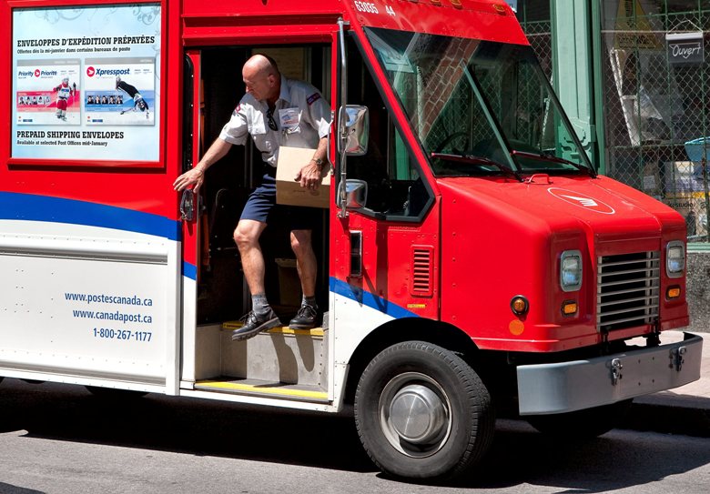 A Canada Post worker gets out of his delivery truck with a box in his hand.