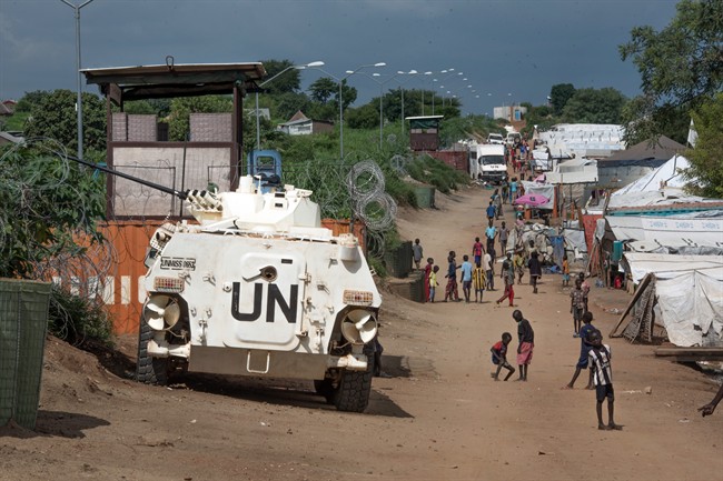 In this photo taken Monday, July 25, 2016, some of the more than 30,000 Nuer civilians sheltering in a United Nations base in South Sudan's capital Juba for fear of targeted killings by government forces walk by an armored vehicle and a watchtower manned by Chinese peacekeepers.