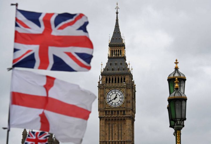 A Union flag flies above an English St. Georges Cross flag near the Big Ben clock face and the Elizabeth Tower at Houses of Parliament in central London on June 29, 2016.