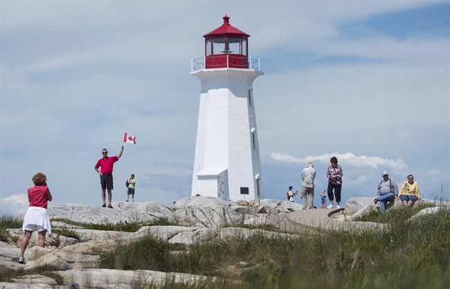 Keith Boutilier, second from left, poses with a Canadian flag for his wife France Boutilier, left, in Peggy's Cove, N.S., on Canada Day, July 1, 2016.