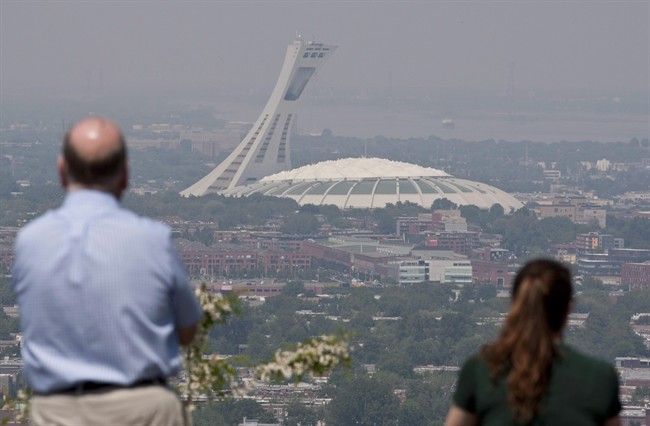 Tourists look through out through smog at Montreal's Olympic Stadium in a May 31, 2010, file photo. It's been dubbed the "Big Owe" for its runaway construction costs and it has attracted widespread derision for falling concrete and roof rips but Montreal's Olympic Stadium doesn't just have detractors.
