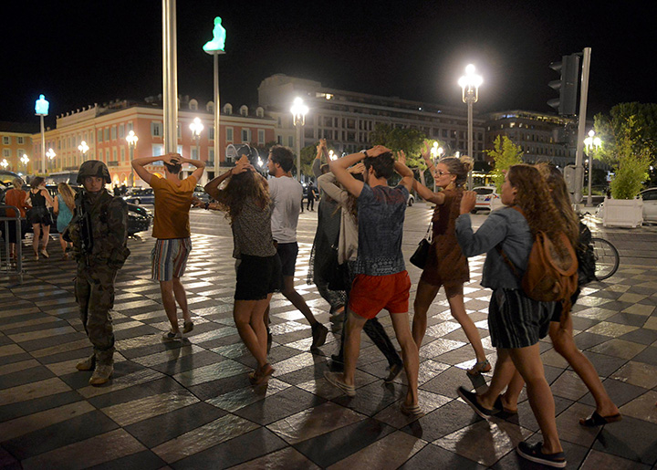 People cross the street with their hands on their heads as a French soldier secures the area after a truck drove into a crowd celebrating the Bastille Day killing at least 80 people along the Promenade des Anglais in Nice, France.