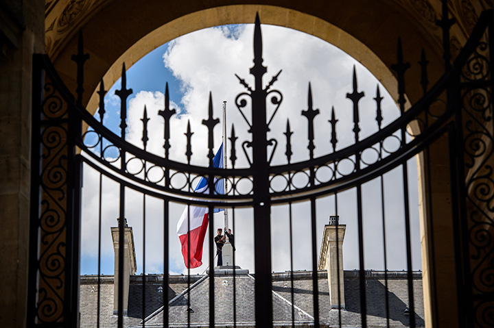 A picture taken through the gate shows French Republican guards placing the French flag at half-staff at the Elysee presidential Palace, in Paris, on July 15, 2016 as French government announced a three days of national mourning after the attack in Nice.