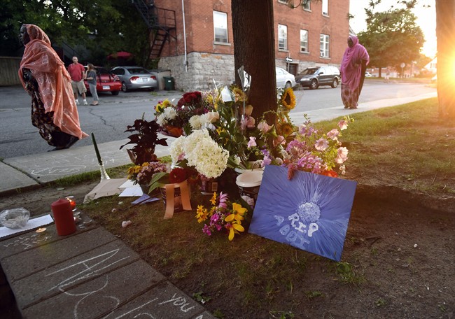 Mourners arriving for a memorial pass flowers laid outside the apartment where Abdirahman Abdi lived and was fatally injured after being arrested by Ottawa Police officers.