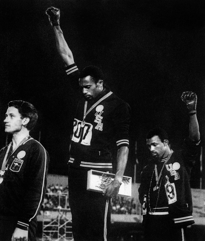 US athletes Tommie Smith (C) and John Carlos (R) raise their gloved fists in the Black Power salute to express their opposition to racism in the USA during the US national anthem, after receiving their medals 17 October 1968.