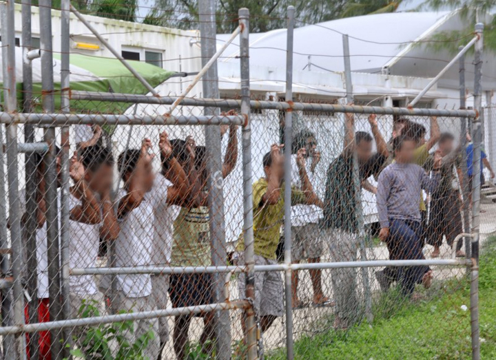 Asylum seekers look at the media from behind a fence at the Manus Island detention centre, Papua New Guinea in this picture taken March 21, 2014.