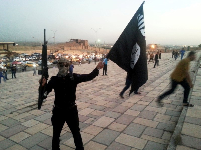 File photo of a fighter of the Islamic State of Iraq and the Levant (ISIL) holds an ISIL flag and a weapon.