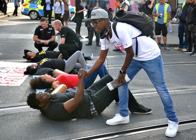 A man shakes hands with one of the activists as they lay on the road outside Nottingham Theatre Royal during an attempt to shut down part of the city centre tram and bus network in Nottingham, England Friday Aug. 5, 2016 to protest for social justice movement Black Lives Matter. 