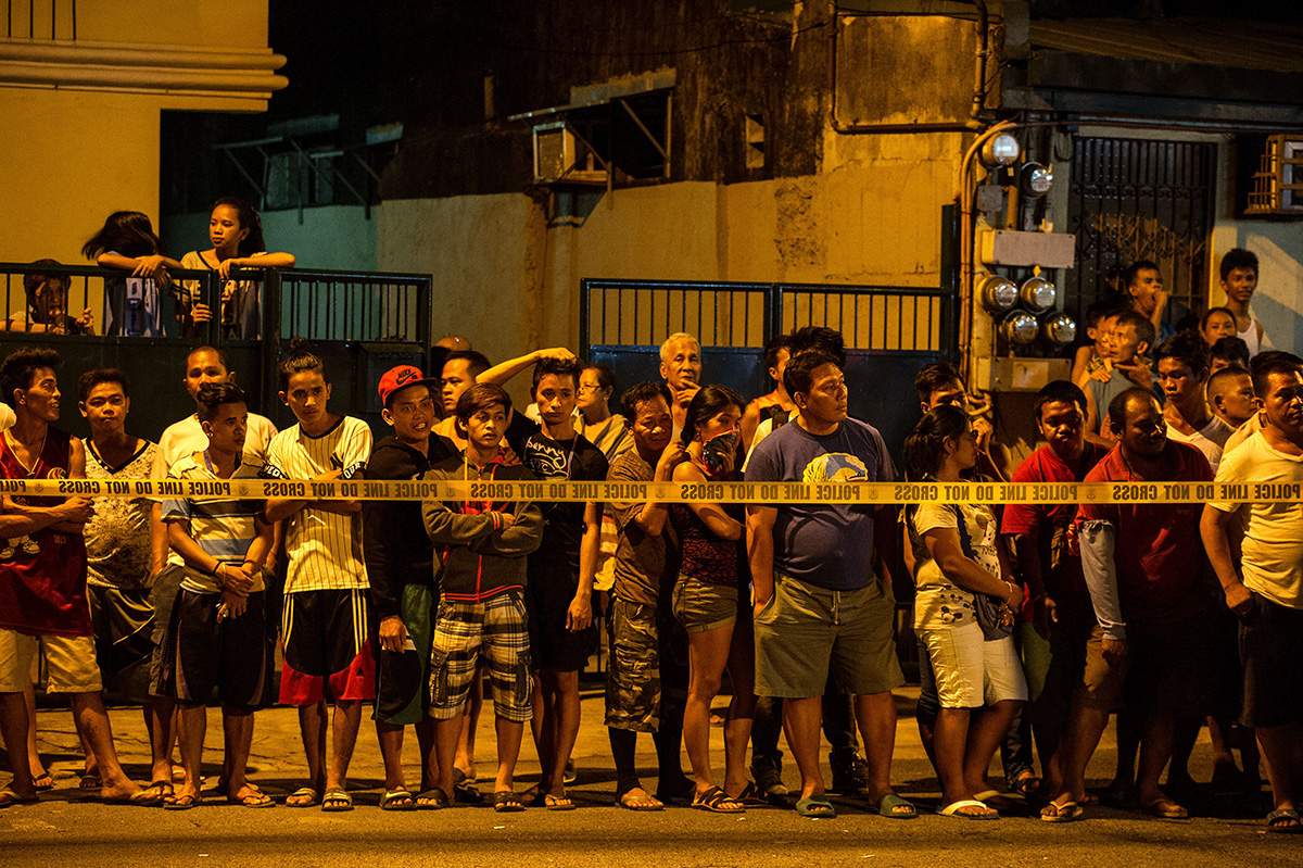 In this photo taken on July 19, 2016, shows residents behind a police line looking at the two dead bodies of an alleged drug dealer after a drug bust operation that turned into a gun fight in Manila. 