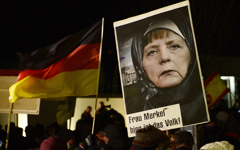 A protestor holds a poster with an image of German Chancellor Angela Merkel wearing a headscarf in front of the Reichstag building with a crescent on top during a rally of the group Patriotic Europeans against the Islamization of the West, or PEGIDA, in Dresden, Germany.  Words on poster read : "Mrs. Merkel, here is the people." .