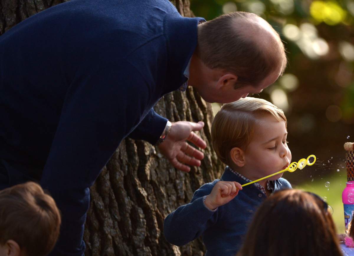Prince George plays with bubbles as Prince William looks on during a children’s tea party at Government House in Victoria, Thursday, Sept. 29, 2016.