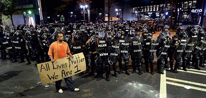 A protester walks in front of CMPD officers in riot gear with a sign reading “All Lives Matter We Are 1” in Charlotte, N.C. Wednesday, Sept. 21, 2016.