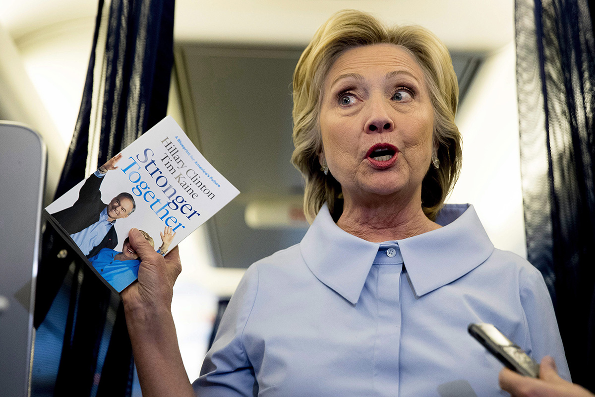 Democratic presidential candidate Hillary Clinton holds up a book entitled "Stronger Together" as she speaks to members of the media on her campaign plane while traveling to Quad Cities International Airport in Moline, Ill., Monday, Sept. 5, 2016.
