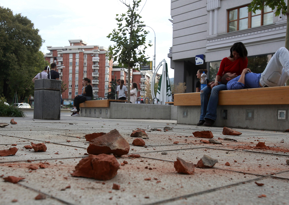 People sit outside buildings near fallen bricks, after an earthquake in Skopje, Macedonia, Sunday, Sept. 11, 2016. 