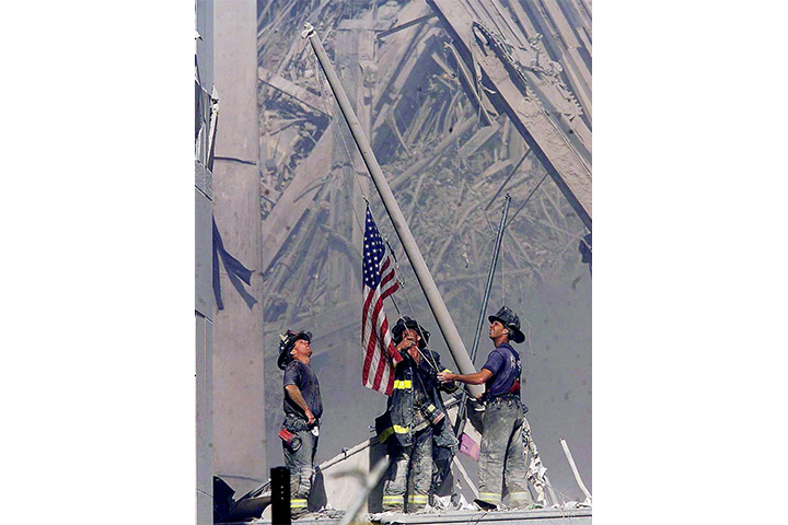 Firefighters raise a flag at the World Trade Center in New York Tuesday, Sept. 11, 2001, as work at the site continues after hijackers crashed two airliners into the center. 
