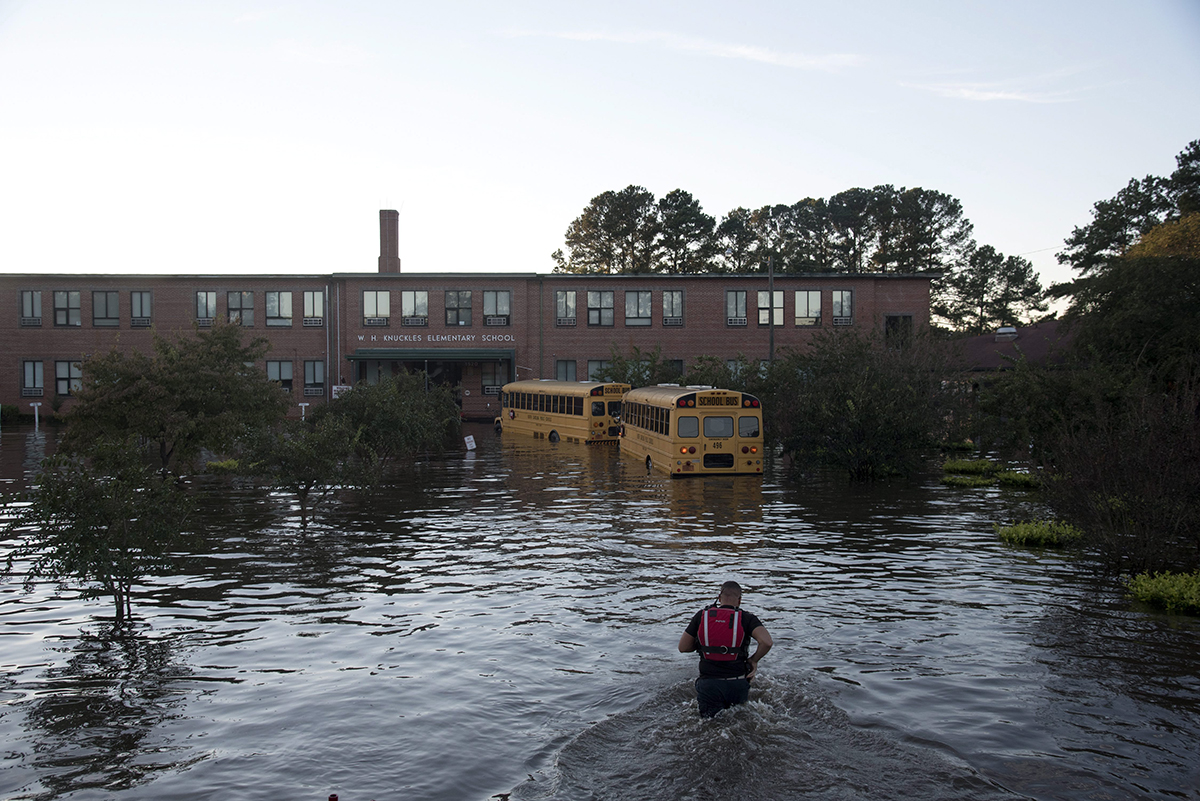 A volunteer firefighter with the Raynham-McDonald Fire Department makes his way through floodwaters caused by rain from Hurricane Matthew to turn off the lights of a school bus in front of W.H. Knuckles Elementary School in Lumberton, N.C., Monday, Oct. 10, 2016.