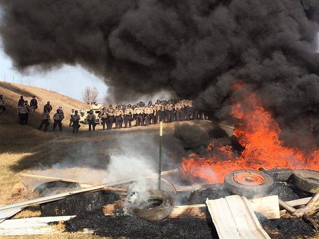 In this Oct. 27, 2016, file photo, tires burn as armed soldiers and law enforcement officers stand in formation to force Dakota Access pipeline protesters off private land in Morton County, N.D., where they had camped to block construction.