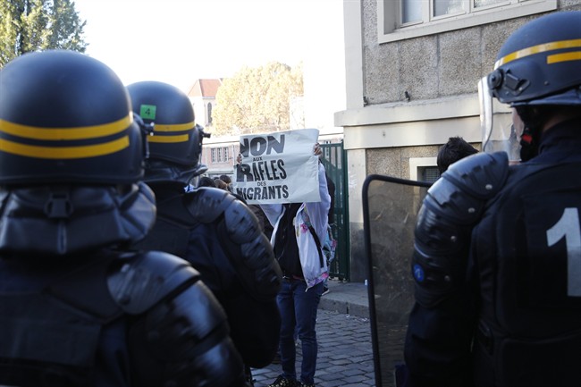 A man holds a poster reading "No to migrants roundup" as police officers control migrants in Paris, Monday, Oct. 31, 2016. 