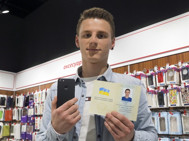 A young man shows his passport giving his name as iPhone Sim (seven), and a new iPhone 7 in an electronics shop in Kiev, Ukraine, Friday, Oct. 28, 2016. 