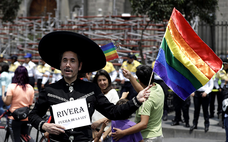 A man dressed as a Mexican cowboy and holding a rainbow flag smiles as he poses for a portrait during a gay rights demonstration outside of Mexico City's Metropolitan Cathedral in Mexico City, Sunday, Sept. 11, 2016. 
