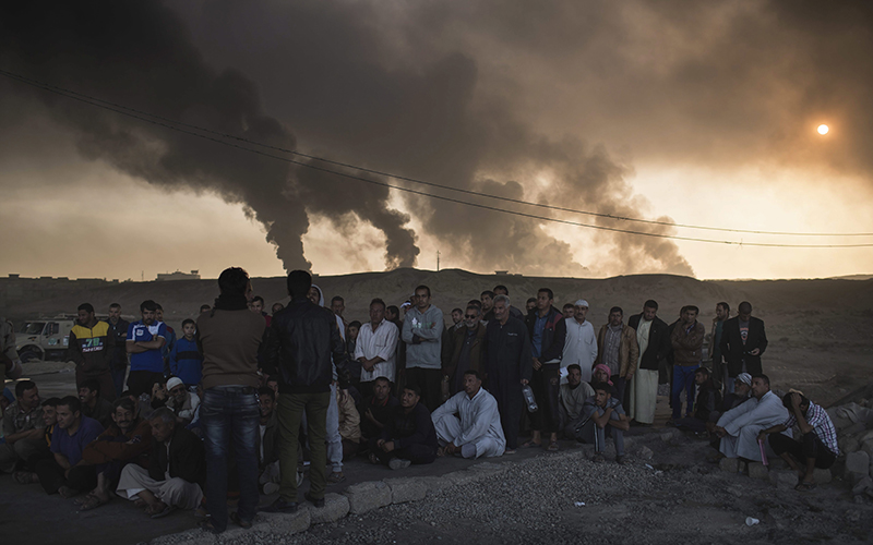 Men are held by Iraqi national security agents, to be interrogated at a checkpoint, as oil fields burn in Qayara, south of Mosul, Iraq, Saturday, Nov. 5, 2016. 