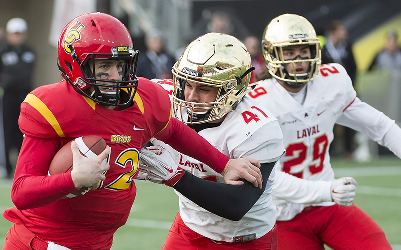 Calgary Dinos quarterback Adam Sinagra fends off Laval Rouge et Or Cedric Lussier-Roy during first half U Sports Vanier Cup championship football action, in Hamilton, Ont., on Saturday, November 26, 2016. 
