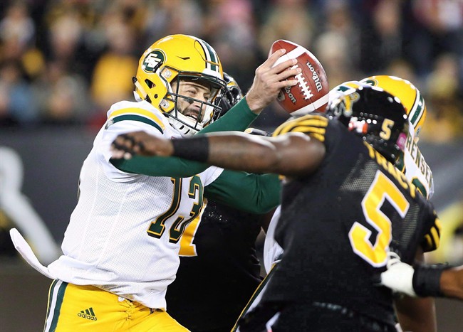 Edmonton Eskimos quarterback Mike Reilly (13) fakes a pass and holds the ball while under pressure from the Hamilton Tiger-Cats Adrian Tracy during the first half of CFL football action in Hamilton on October 28, 2016. 