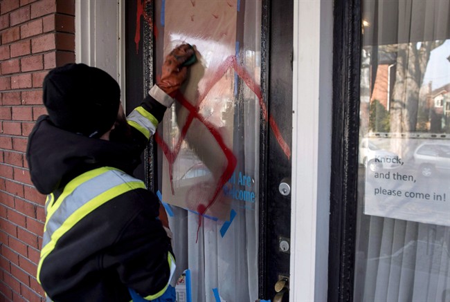 A graffiti removal worker cleans anti-Semitic graffiti, including a swastika, that was spray painted on the door of The Glebe Minyan in Ottawa, on Tuesday, Nov. 15, 2016.