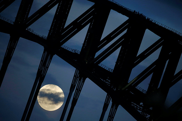 People on the Sydney Harbour Bridge Climb (R) walk down the western span of the famous Australian landmark as the supermoon rises through clouds after sunset, November 14, 2016.