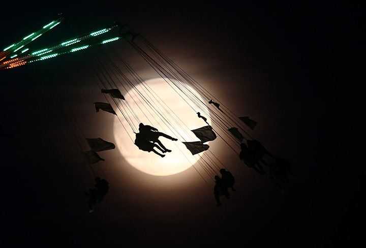 People on a funfair ride are silhouetted against the moon, in London, November 13, 2016.