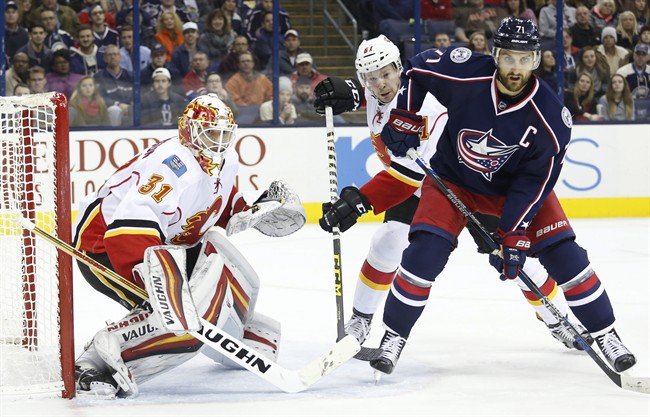 Calgary Flames' Chad Johnson, left, protects the net as teammate Brett Kulak, center, and Columbus Blue Jackets' Nick Foligno look for the puck during the second period of an NHL hockey game Wednesday, Nov. 23, 2016, in Columbus, Ohio. 