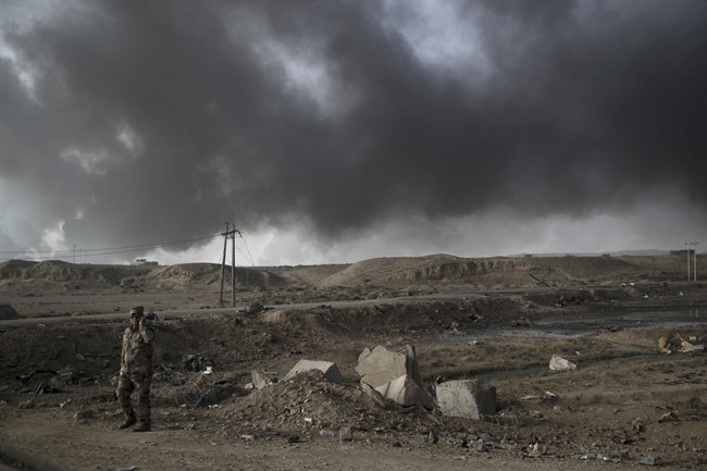 A Iraqi soldier stands near a checkpoint as smoke rises from burning oil fields in Qayara, south of Mosul, Iraq, Tuesday, Nov. 1, 2016. 