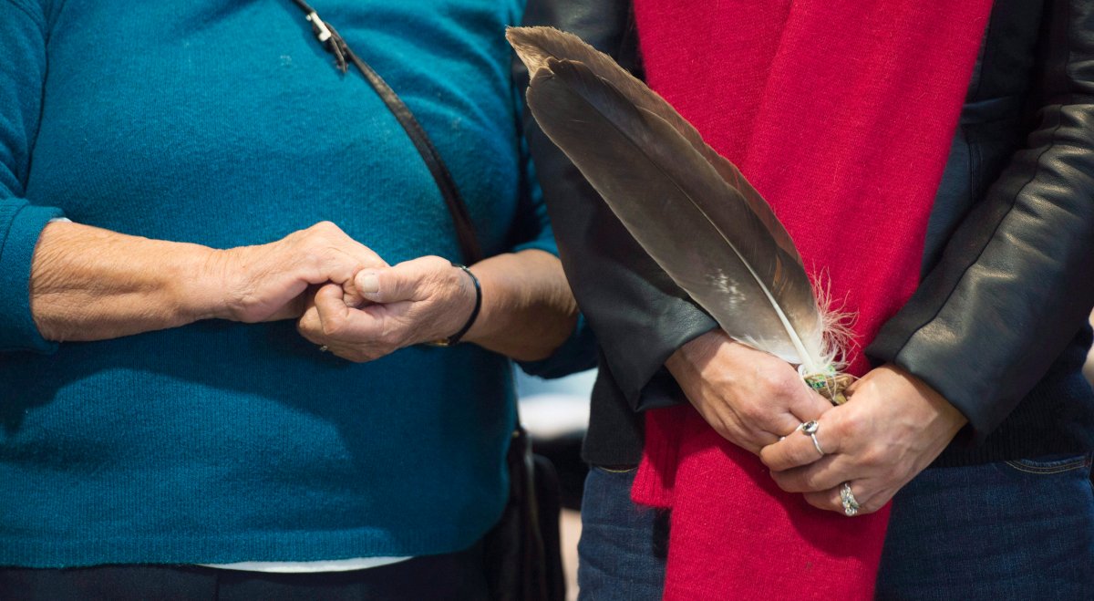 Two First Nations women stand side-by-side holding a feather in Kahnawake, Que.