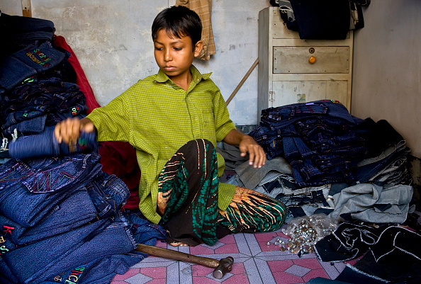 A child laborer at work in a small garment factory, where he works on the finishing stages of making blue jeans. (Photo by ANDREW HOLBROOKE/Corbis via Getty Images).