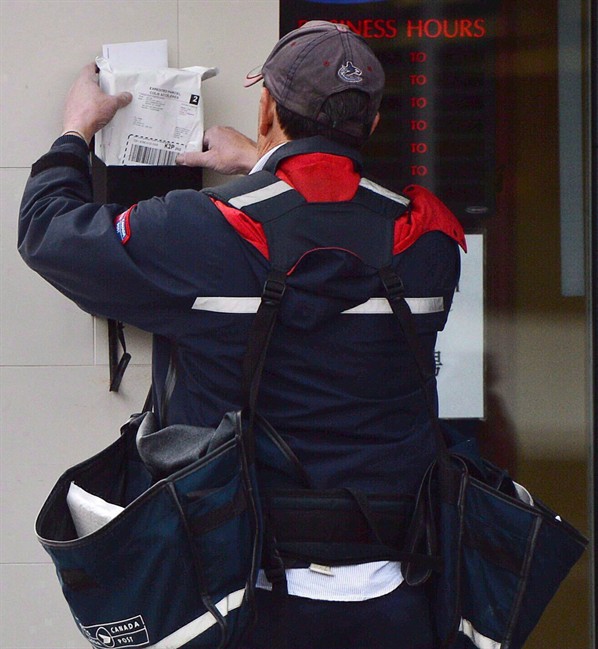 A mail carrier delivers mail in Ottawa, on Dec.11, 2013. A House of Commons committee is recommending Canada Post come up with a plan to reinstate door-to-door delivery in parts of the country that lost the service in the last year and maintain a freeze on the installation of community mailboxes. 
