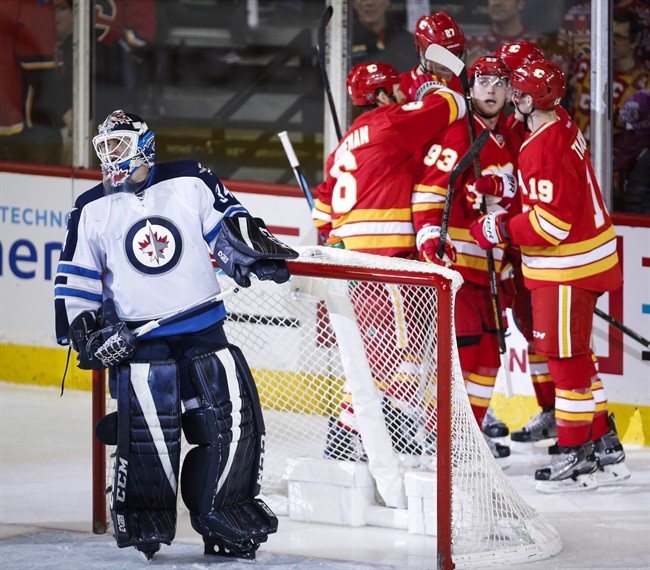 Winnipeg Jets goalie Michael Hutchinson, left, looks away as Calgary Flames celebrate their fourth goal during second period NHL hockey action in Calgary, Saturday, Dec. 10, 2016.