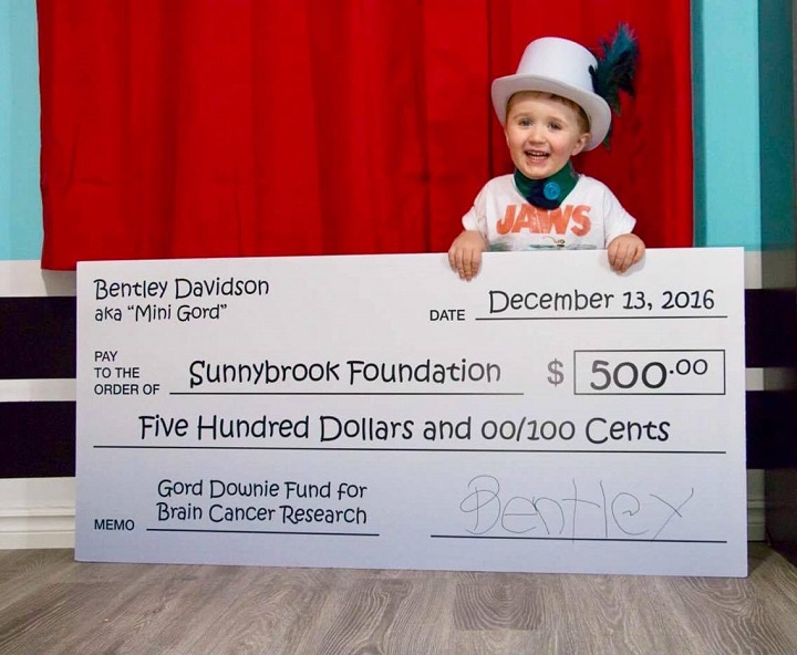 Bentley Davidson, also known as "Mini Gord Downie," smiles as he presents a $500 cheque to Sunnybrook Hospital in honour of his hero. 