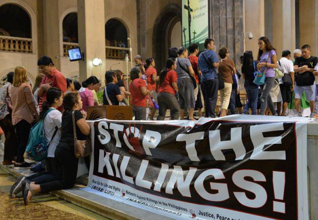 Catholic faithful receive communion next to a tarpaulin with an 'anti-extra judicial killings' slogan during a mass offered for all the victims of extra judicial killings, at a church in Manila on November 23, 2016.