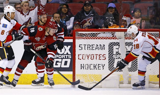Arizona Coyotes center Christian Dvorak (18) scores a goal past Calgary Flames center Matt Stajan (18) and defenseman Dennis Wideman (6) while Coyotes right wing Josh Jooris (86) looks on during a first period of an NHL hockey game Monday, Dec. 19, 2016, in Glendale, Ariz. 