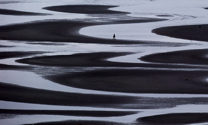 A woman walks through a tidal pool along the shore of Semiahmoo Bay during low tide in White Rock, B.C., on March 11, 2016.