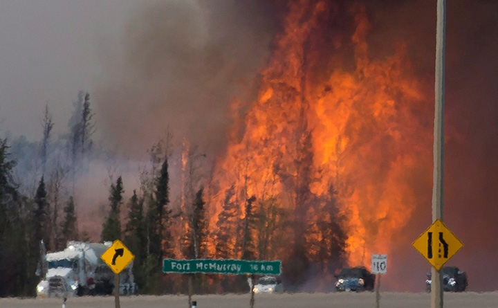Heat waves are seen as cars and trucks drive past a wildfire south of Fort McMurray, Alberta on May 6, 2016. 