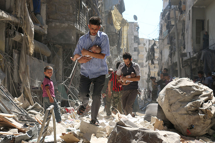 Syrian men carrying babies make their way through the rubble of destroyed buildings following a reported air strike on the rebel-held Salihin neighbourhood of Aleppo on September 11, 2016. 