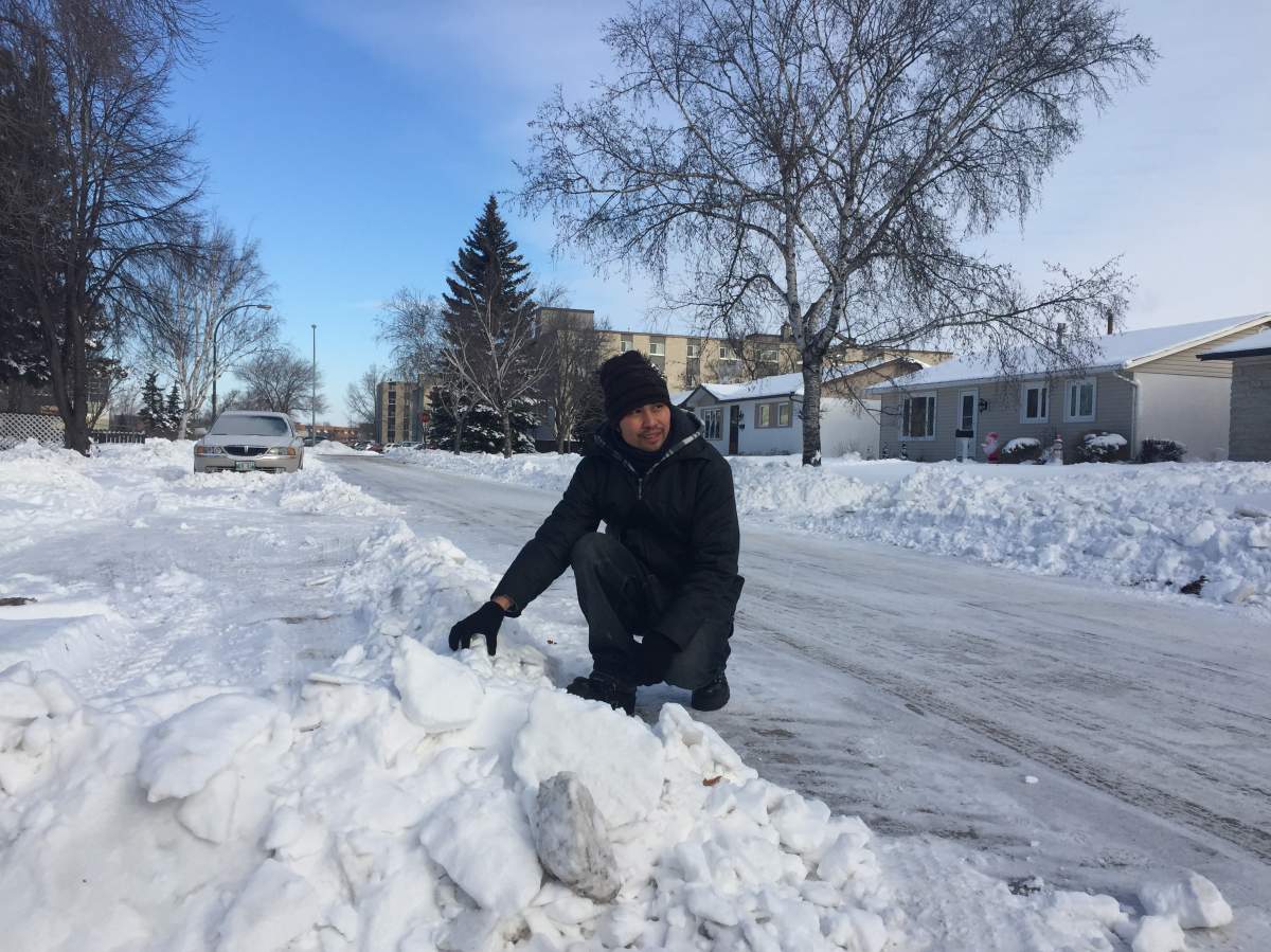 Rusky Collantes kneels on his street beside large snow ruts after residential plowing.