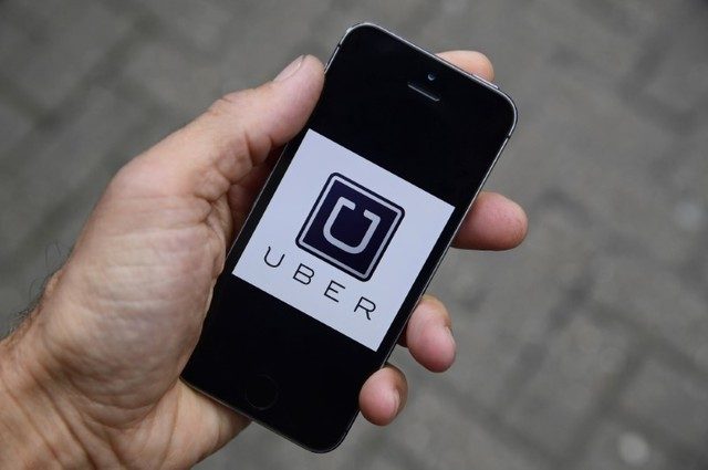 A photo illustration shows the Uber app logo displayed on a smartphone, as it is held up for a posed photograph.