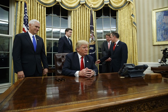 Vice President Mike Pence, left, watches as President Donald Trump prepares to sign his first executive order, Friday, Jan. 20, 2017, in the Oval Office of the White House in Washington. (AP Photo/Evan Vucci).